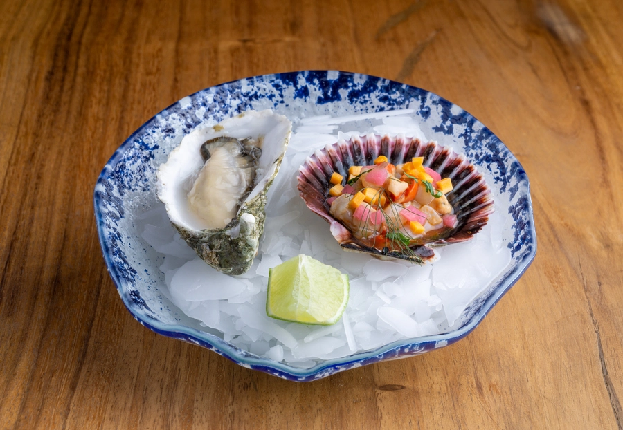 Plato de mariscos frescos con ostra y vieira en un plato de cerámica azul, acompañado de hielo y una rodaja de lima en escapada cultural a Toledo