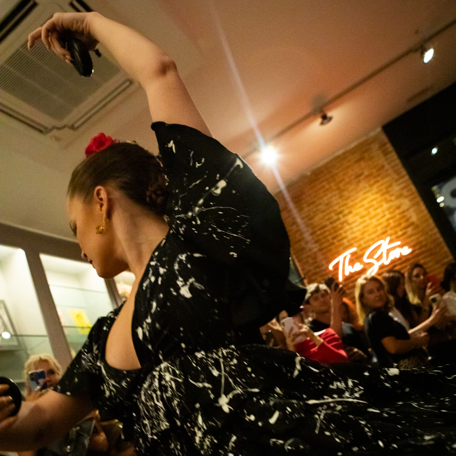 Bailaora de flamenco en Madrid actuando con castañuelas, luciendo un vestido negro con detalles blancos y una flor roja en el cabello, en un espacio moderno con público y ambiente íntimo en el Centro Cultural Flamenco de Madrid