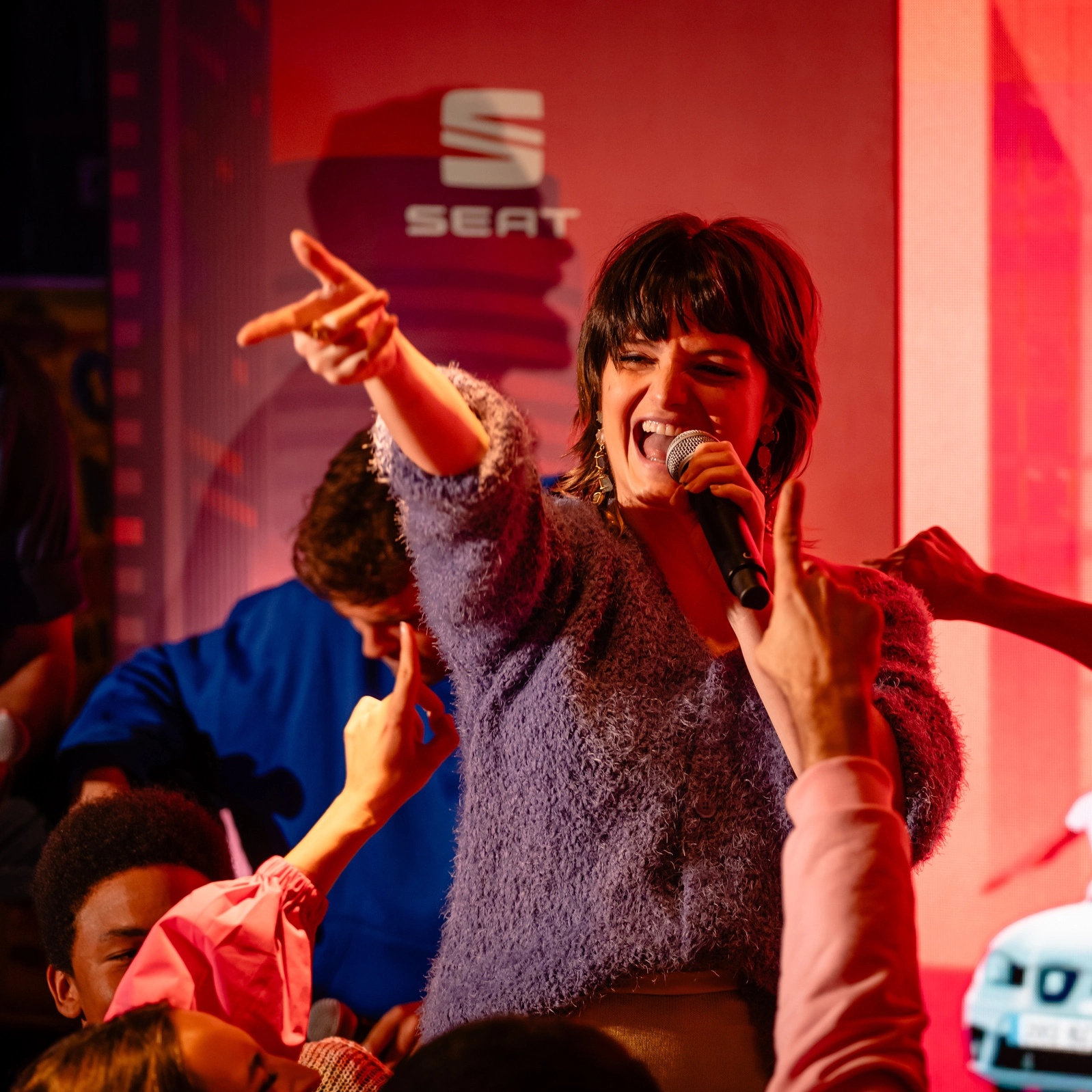 Mujer cantando apasionadamente al micrófono en un evento de SEAT, rodeada de una multitud energética