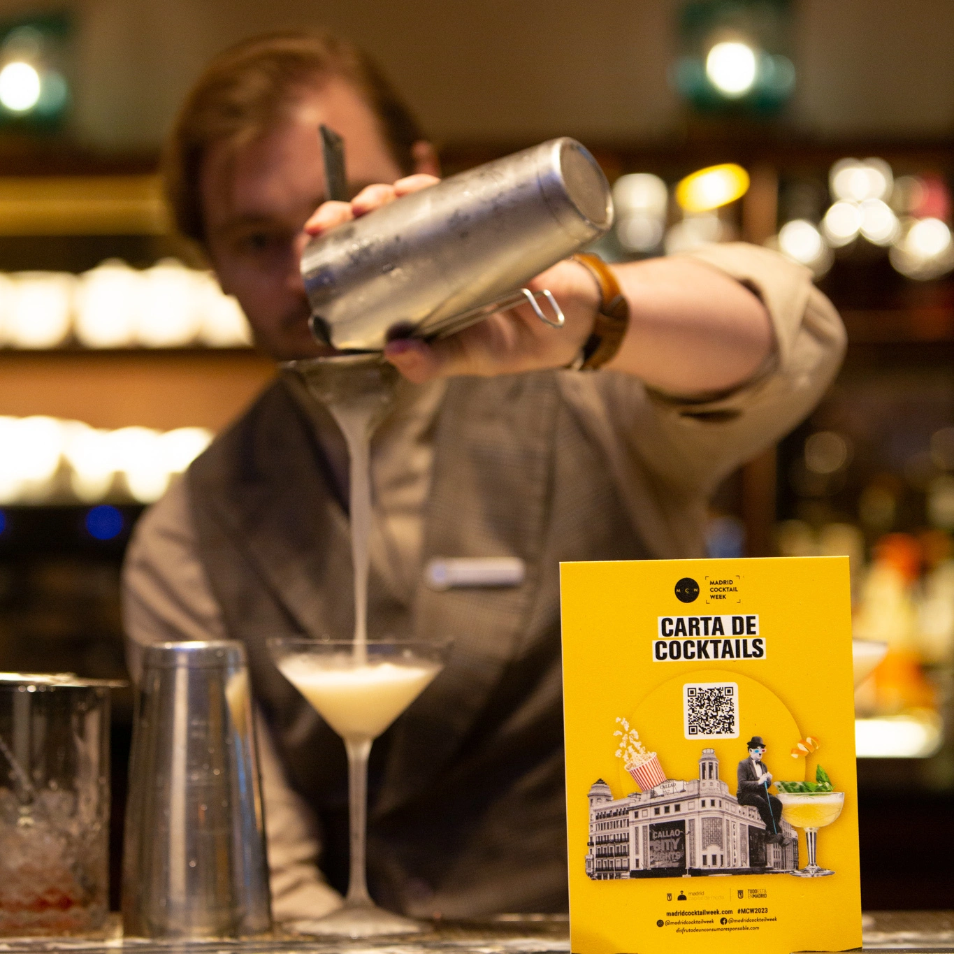 Bartender preparando un cóctel en una coctelería elegante, con una carta de cócteles destacada en primer plano. Ambiente sofisticado y moderno en Madrid Cocktail Week