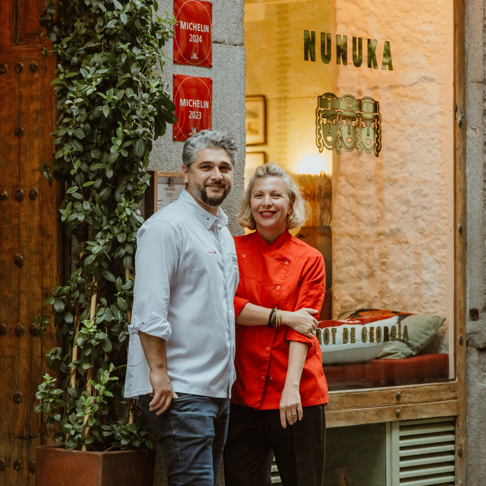 Un hombre y una mujer con un mandil de chef sonriendo frente a un restaurante con fachada tradicional y acogedora