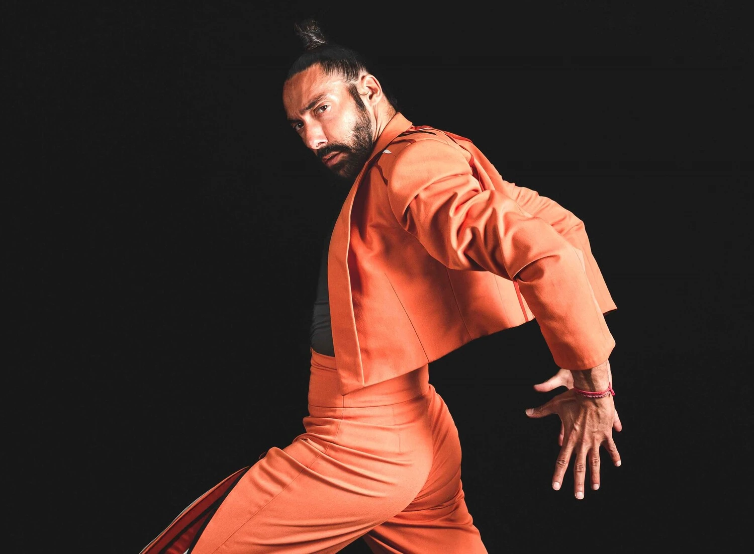 ailarín de flamenco en Madrid con traje naranja, capturado en una pose dramática sobre un fondo negro, resaltando la fuerza y el dinamismo del arte flamenco moderno.