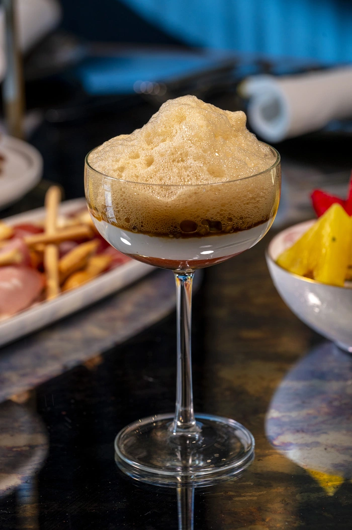 Cóctel servido en una copa elegante con espuma abundante, acompañado de aperitivos y frutas en un ambiente de alta cocina en un brunch con vistas en Madrid