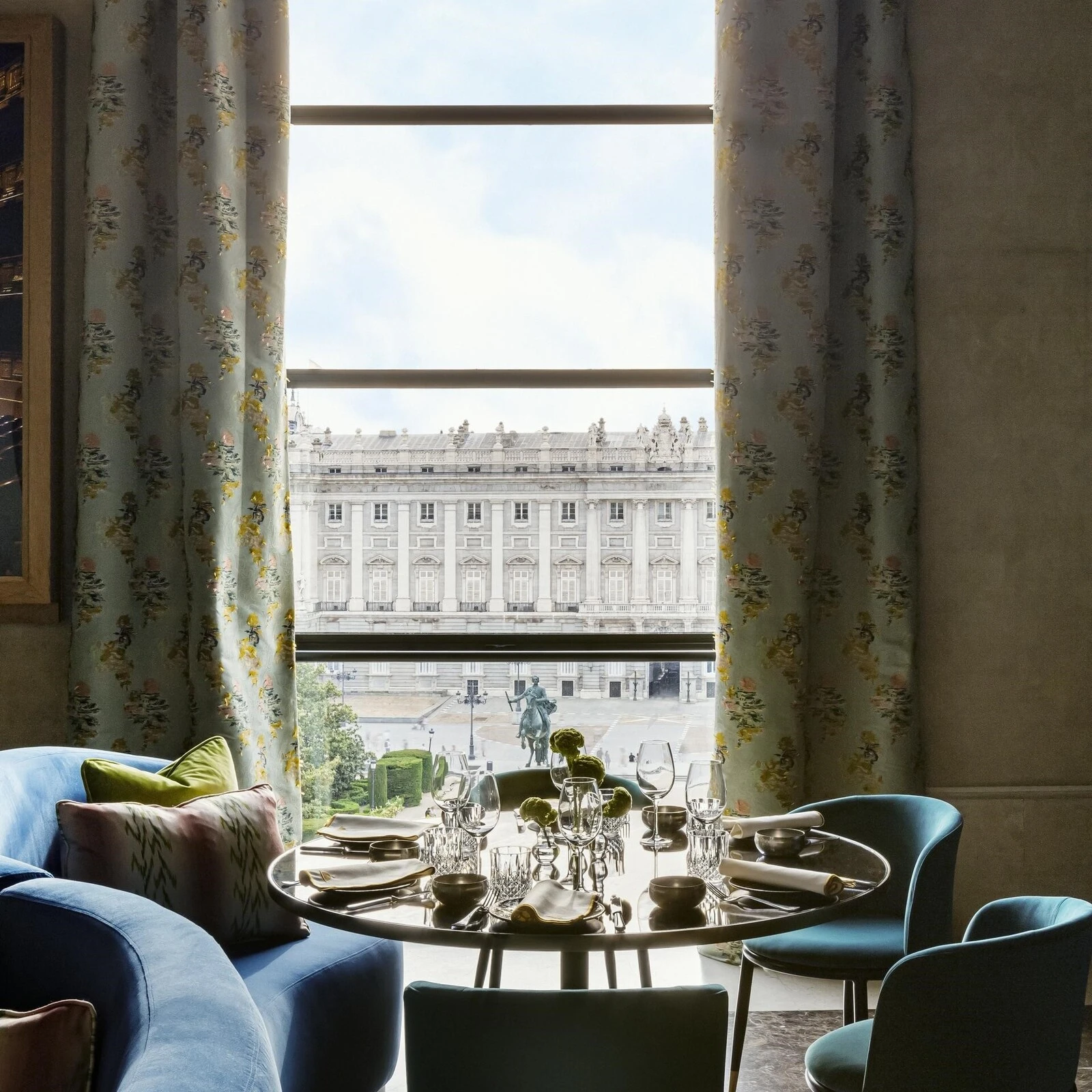 Mesa de comedor elegante con vista al Palacio Real de Madrid, rodeada de sillas modernas y decorada con vajilla fina en un ambiente lujoso y cómodo